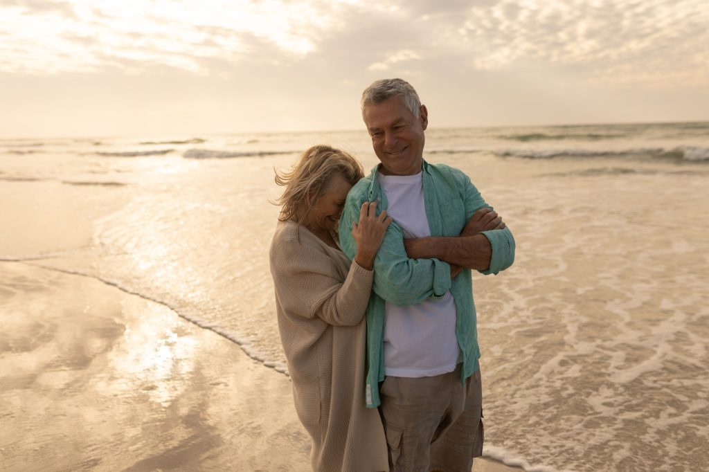 front view of active senior woman embracing senior woman on the beach at dusk